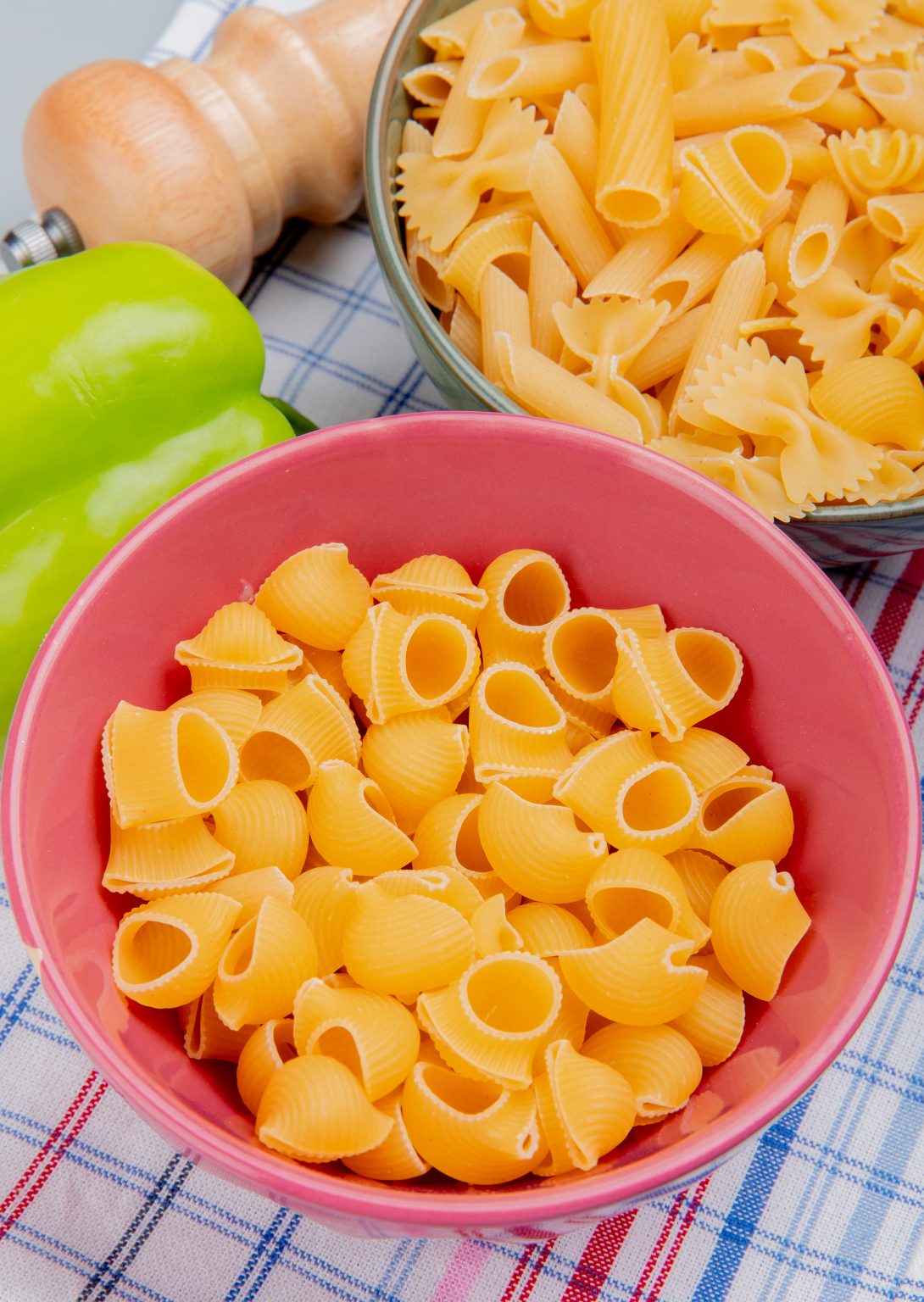 side view of different types of macaroni as pipe-rigate and others with pepper salt on plaid cloth background